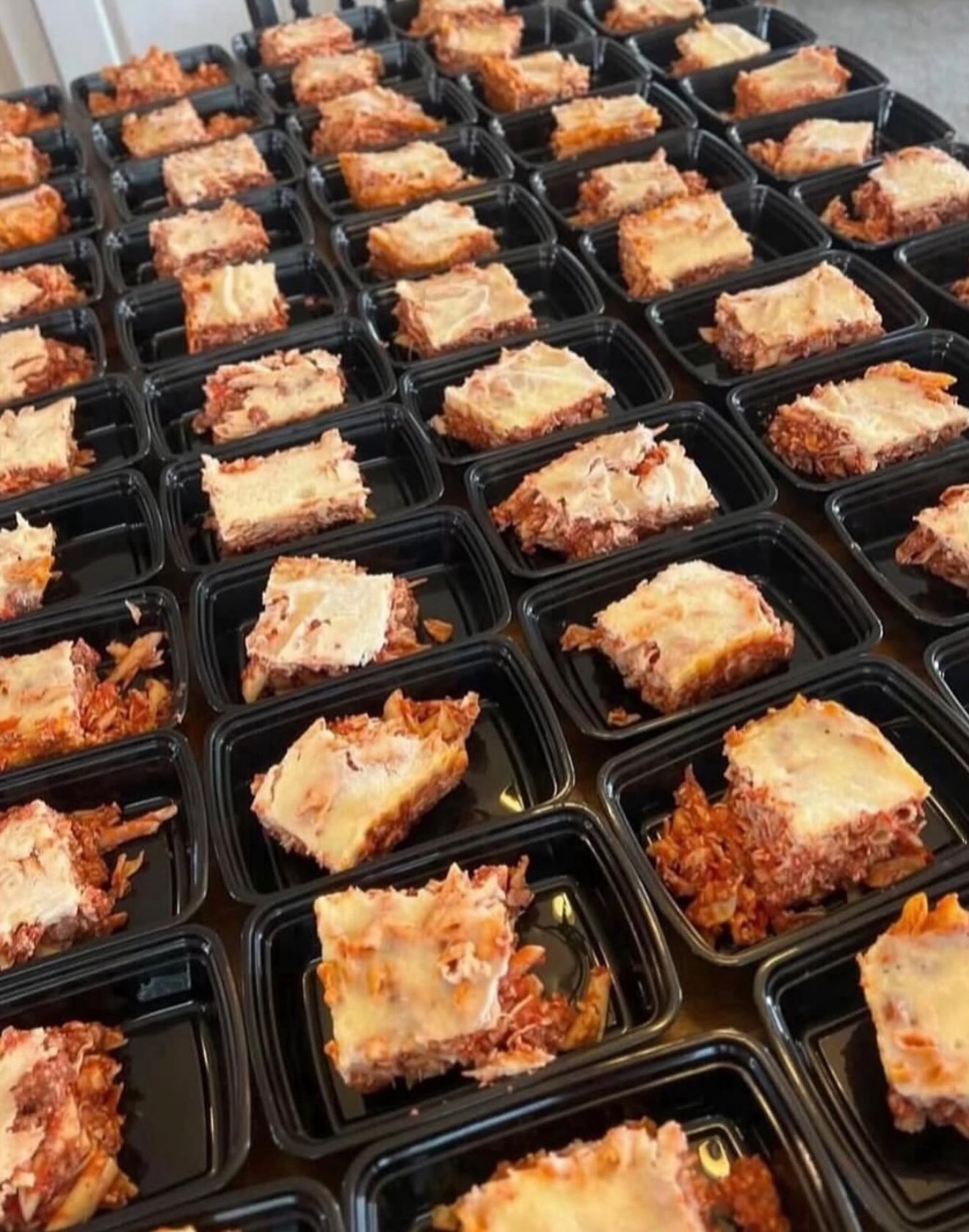 Portions of cheesy baked ziti in black meal-prep trays