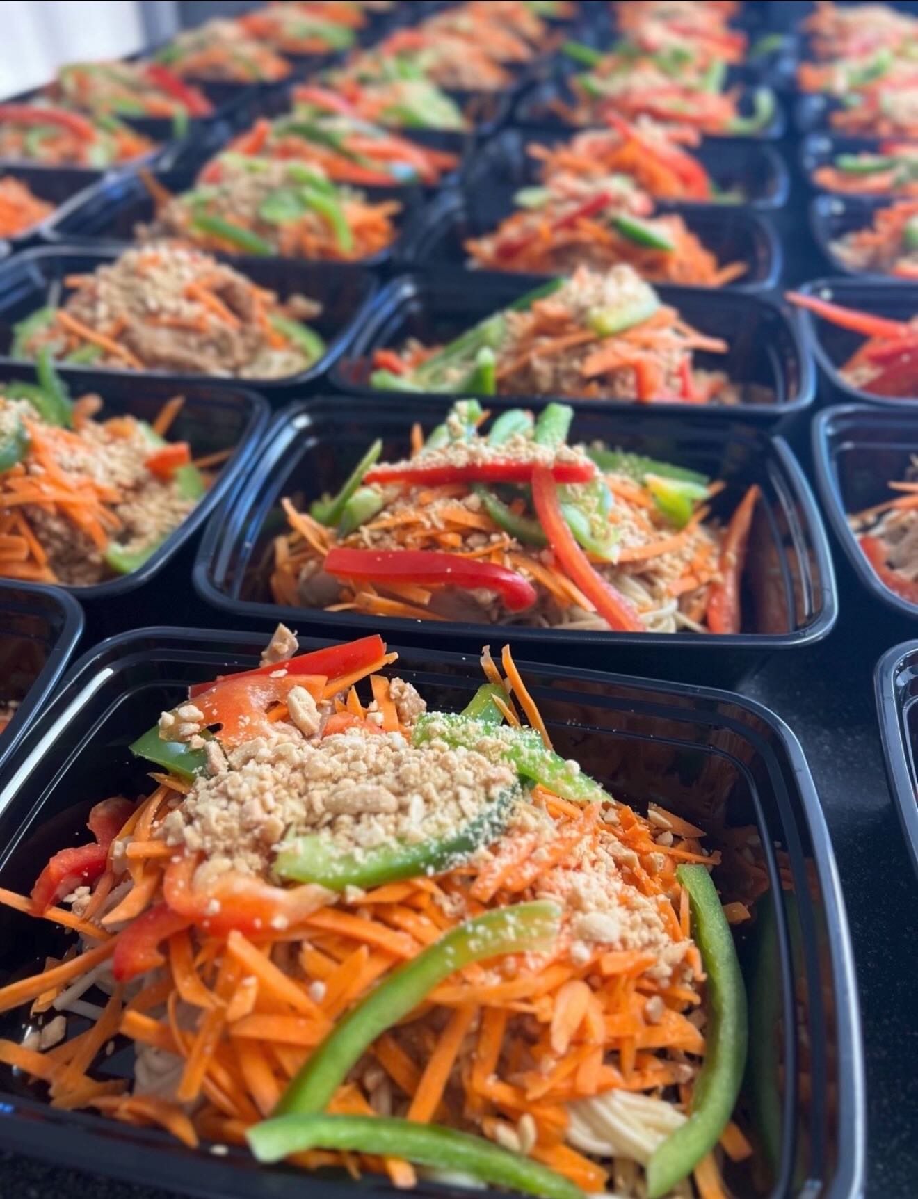 Peanut noodle chicken bowls topped with shredded carrots, bell peppers and crushed peanuts